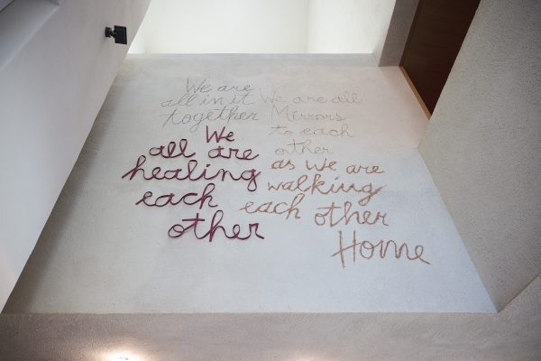 Das Bild zeigt das Kunstwerk "Matter of Change" von Arianna Moroder aus dem Jahr 2023 in der Stadtbibliothek Brixen. Das Werk will durch in Material geschriebene Worte mit seinem / r Betrachter*in über die Wahrnehmung, das Verständnis und die Symbolik von Worten sprechen und daran erinnern, dass Worte keine abstrakten Konzepte sind, sondern das mächtige Rohmaterial unseres täglichen Lebens. Das Kunstwerk zeigt folgenden Text: We are all in it together; We are all healing each other; We are all Mirrors to each other; as we are walking each other Home.