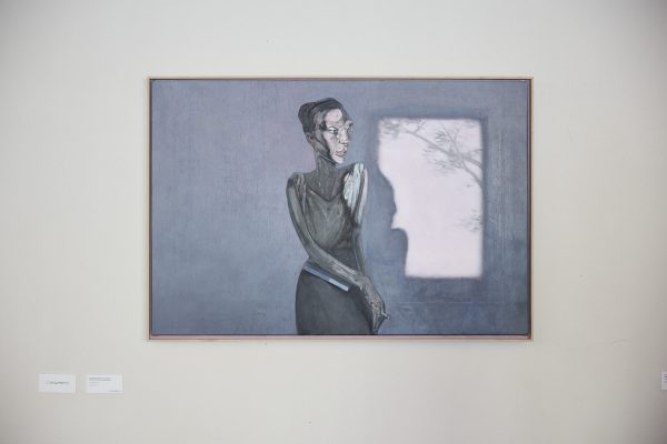 Gemälde von Alessandro Del Pero mit dem Titel „La lettrice“ (2017). Es zeigt eine abstrahierte, in Grautönen gehaltene Frauenfigur mit langen Armen vor einem bläulich-grauen Hintergrund, neben einem hell erleuchteten Fenster, das den Schatten ihres Profils und einen Ast andeutet.